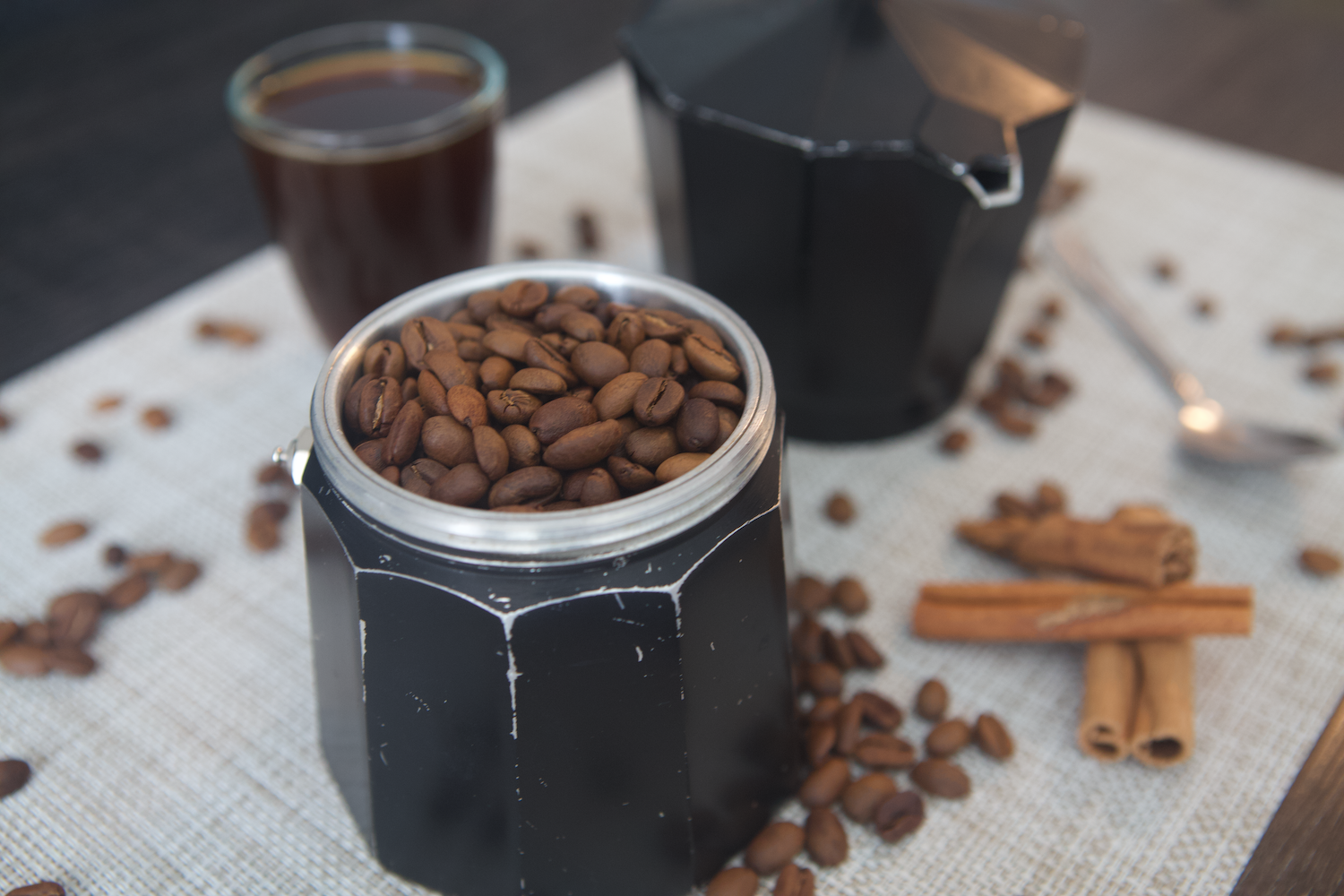 Coffee beans in a moka with an espresso behind it and coffee beans around it