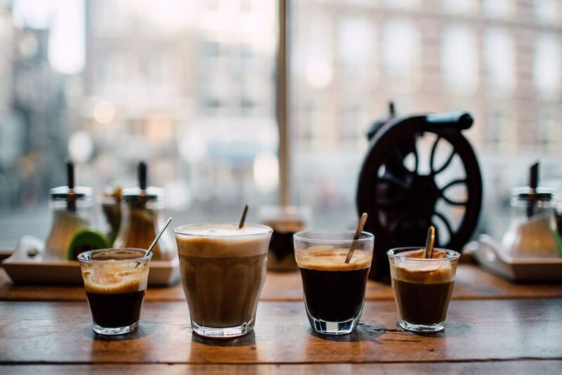 Four coffee drinks on a wooden table near a window