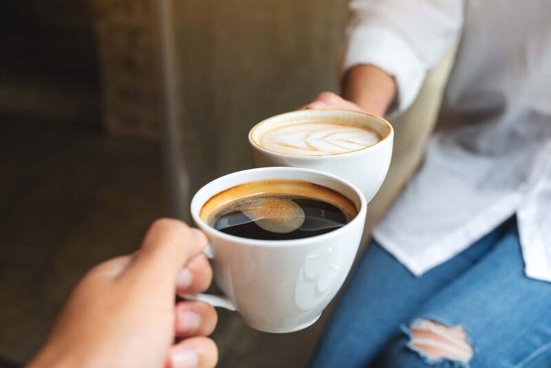Two hands holding coffee cups, one black, one latte.